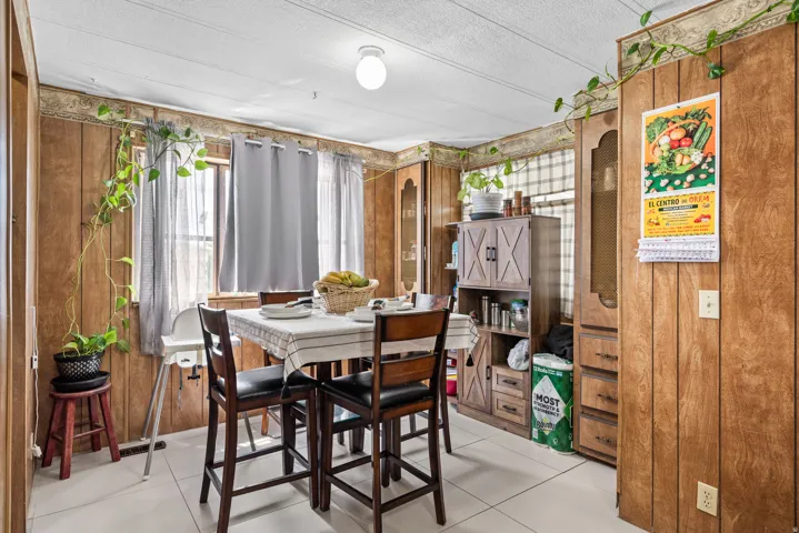 Dining area featuring wood-panel walls, light-colored tile flooring, and a window with sheer and blackout curtains