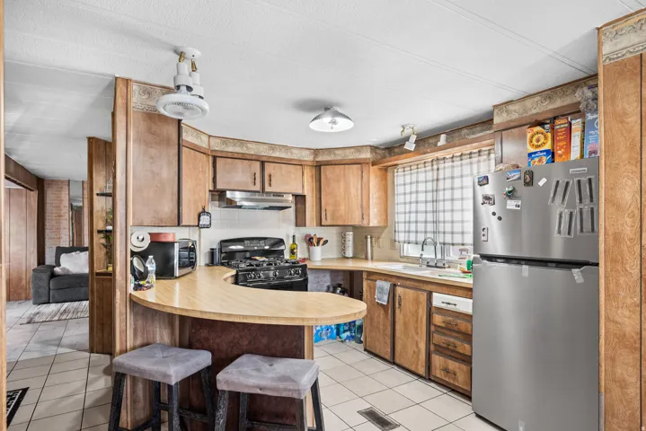 Kitchen featuring wood-finish cabinetry, a curved breakfast bar, a stainless steel refrigerator, a gas range, and tile flooring