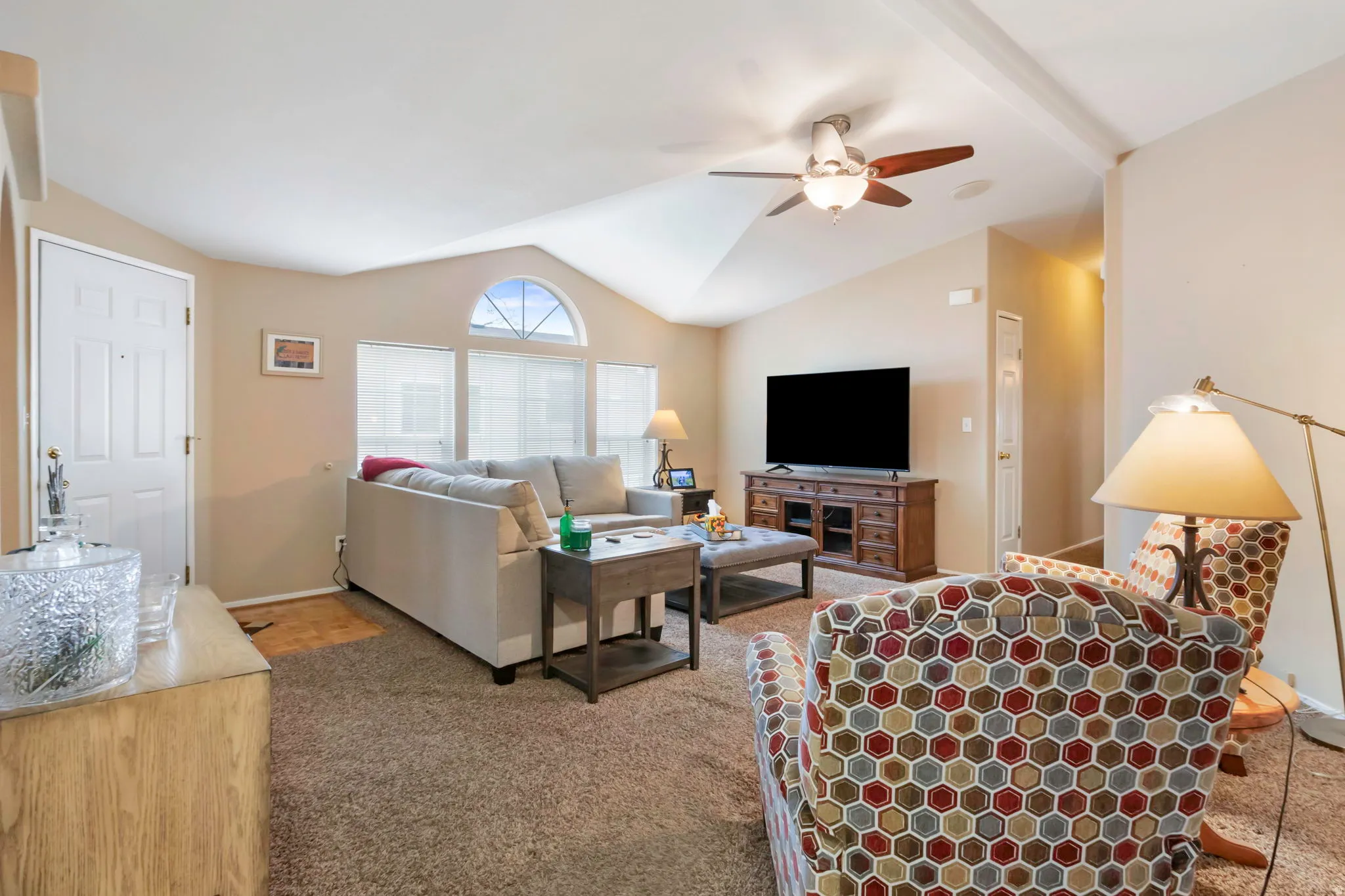 Spacious living area featuring a vaulted ceiling with exposed beams, an arched transom window, and a ceiling fan