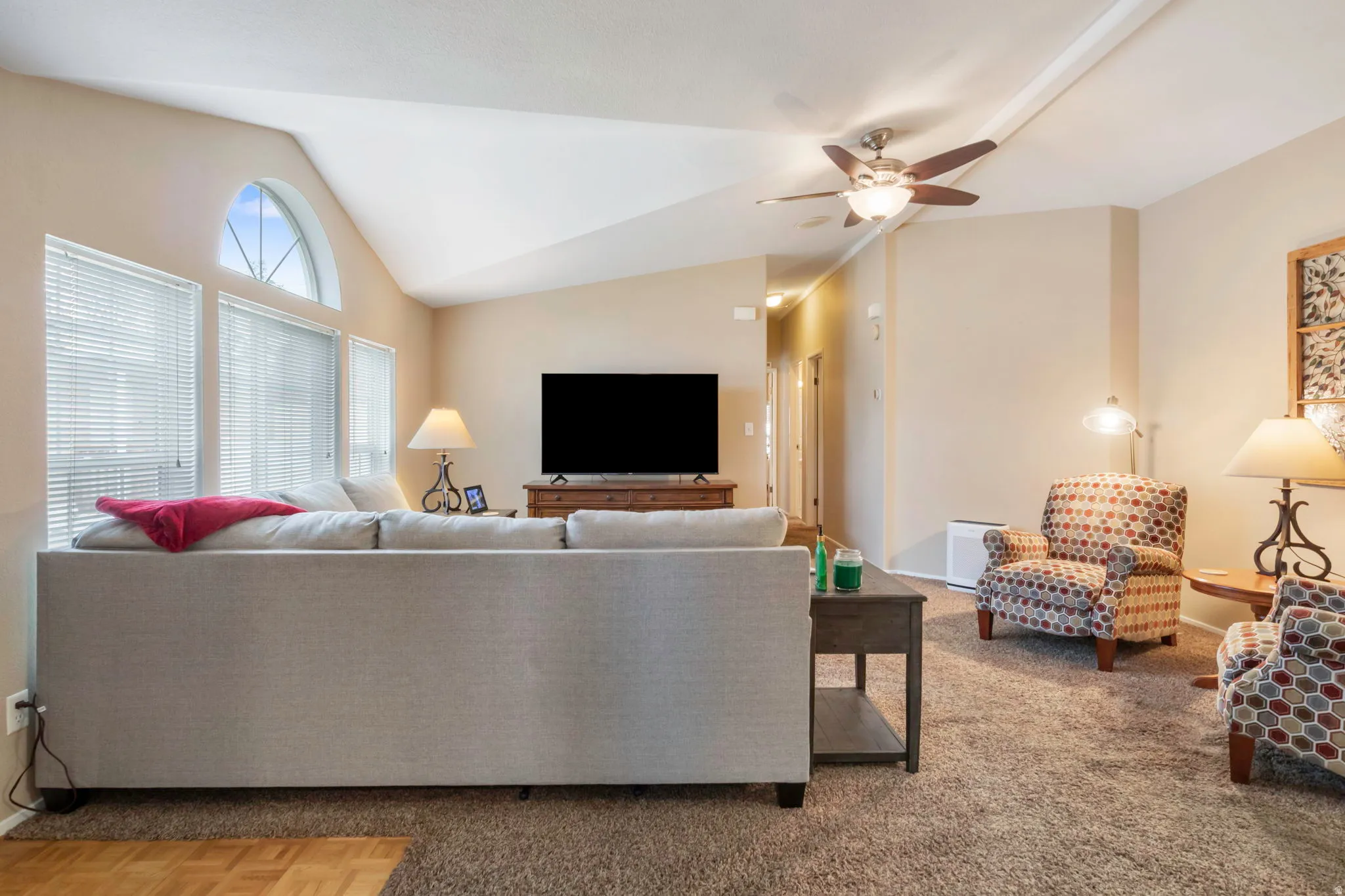 Living area featuring vaulted ceilings with a ceiling fan, arched transom window, and neutral wall tones