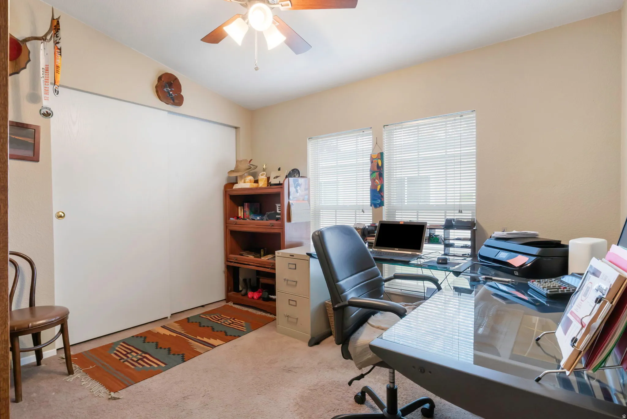 Carpeted room featuring a ceiling fan with light fixture, dual windows with blinds, and white bi-fold closet doors