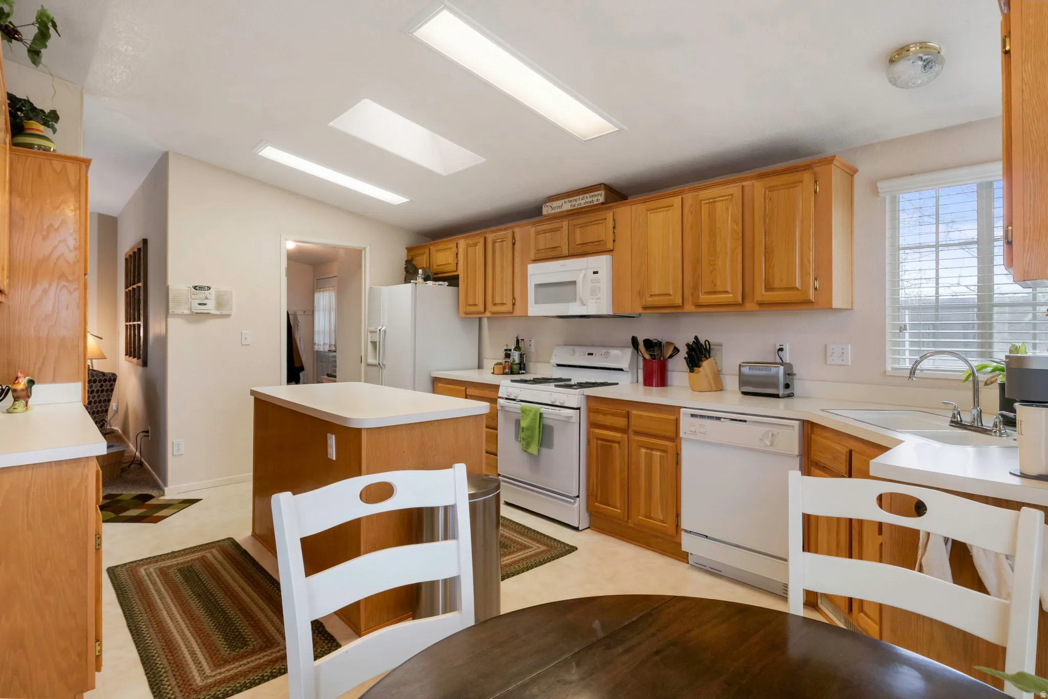 Kitchen featuring light wood cabinetry, white appliances, a center island with a light countertop, and skylights