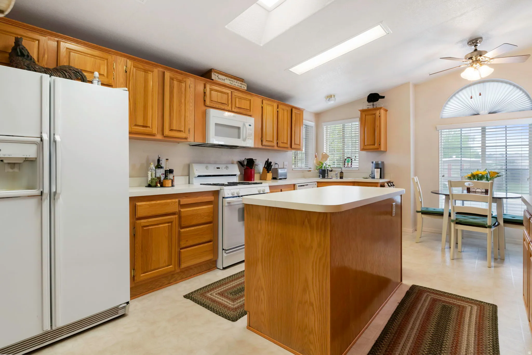 Kitchen featuring wood cabinetry, white countertops, a central island, and a dining area with ample natural light from multiple windows