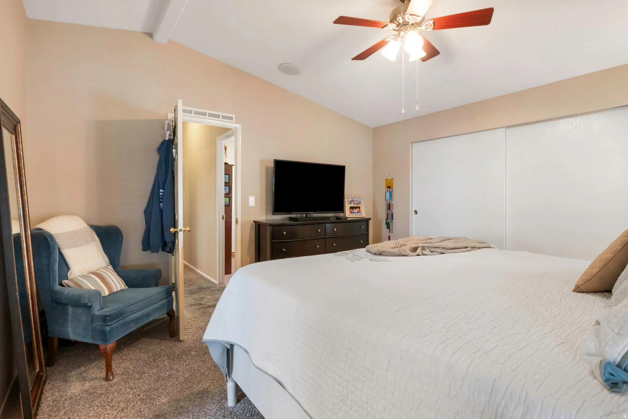 Vaulted ceiling with exposed beam, ceiling fan light fixture, carpeted flooring, and sliding closet doors