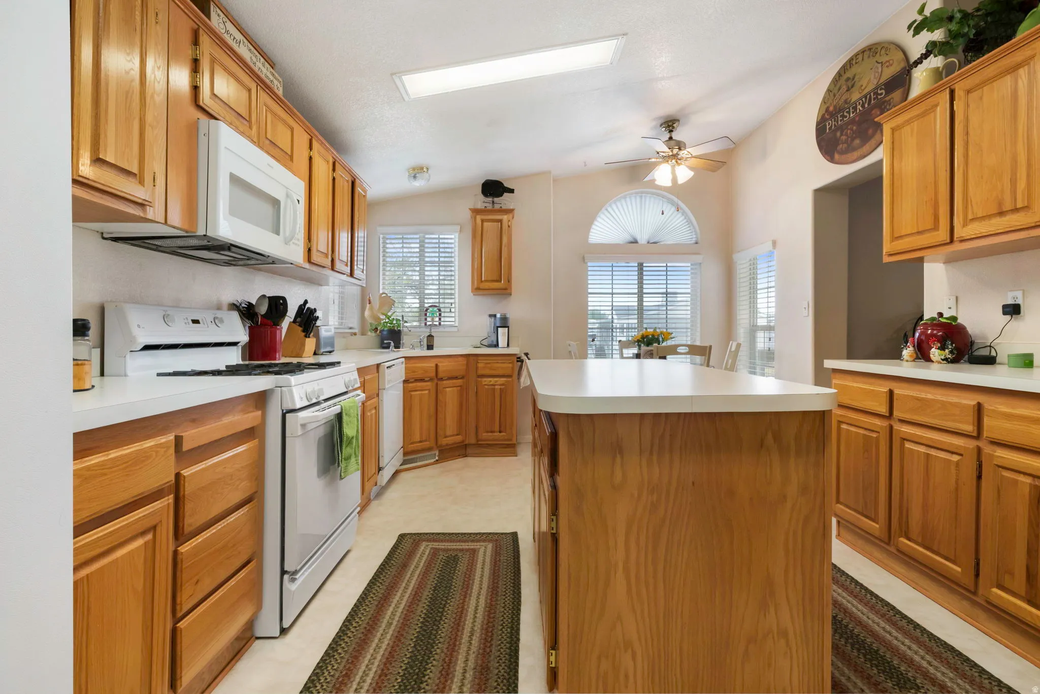 Kitchen featuring wood cabinetry, white countertops, built-in appliances, a central island, and a vaulted ceiling with a skylight