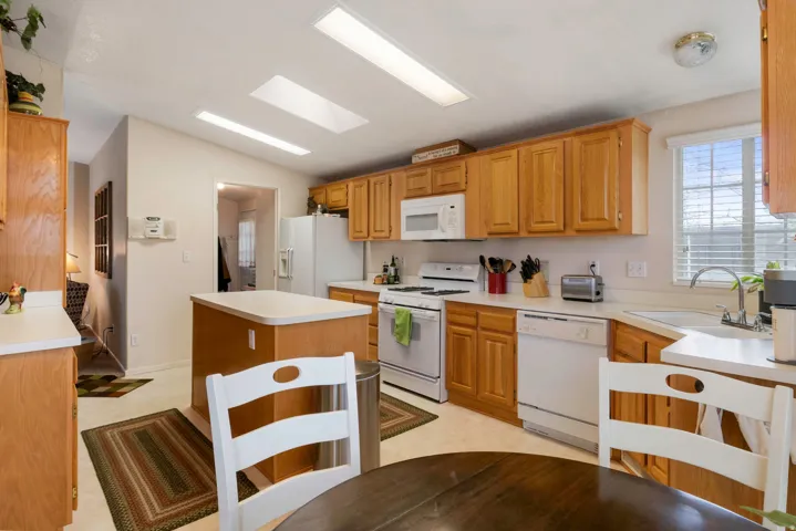 Kitchen featuring light wood cabinetry, white appliances, a center island with a light countertop, and skylights