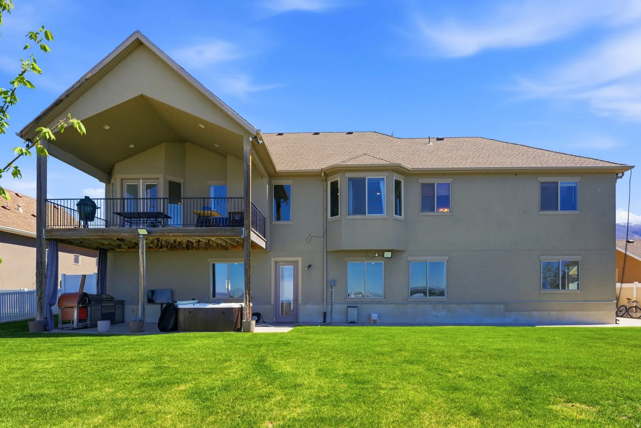 Back of house with a hot tub, stucco siding, a lawn, a patio, and a balcony