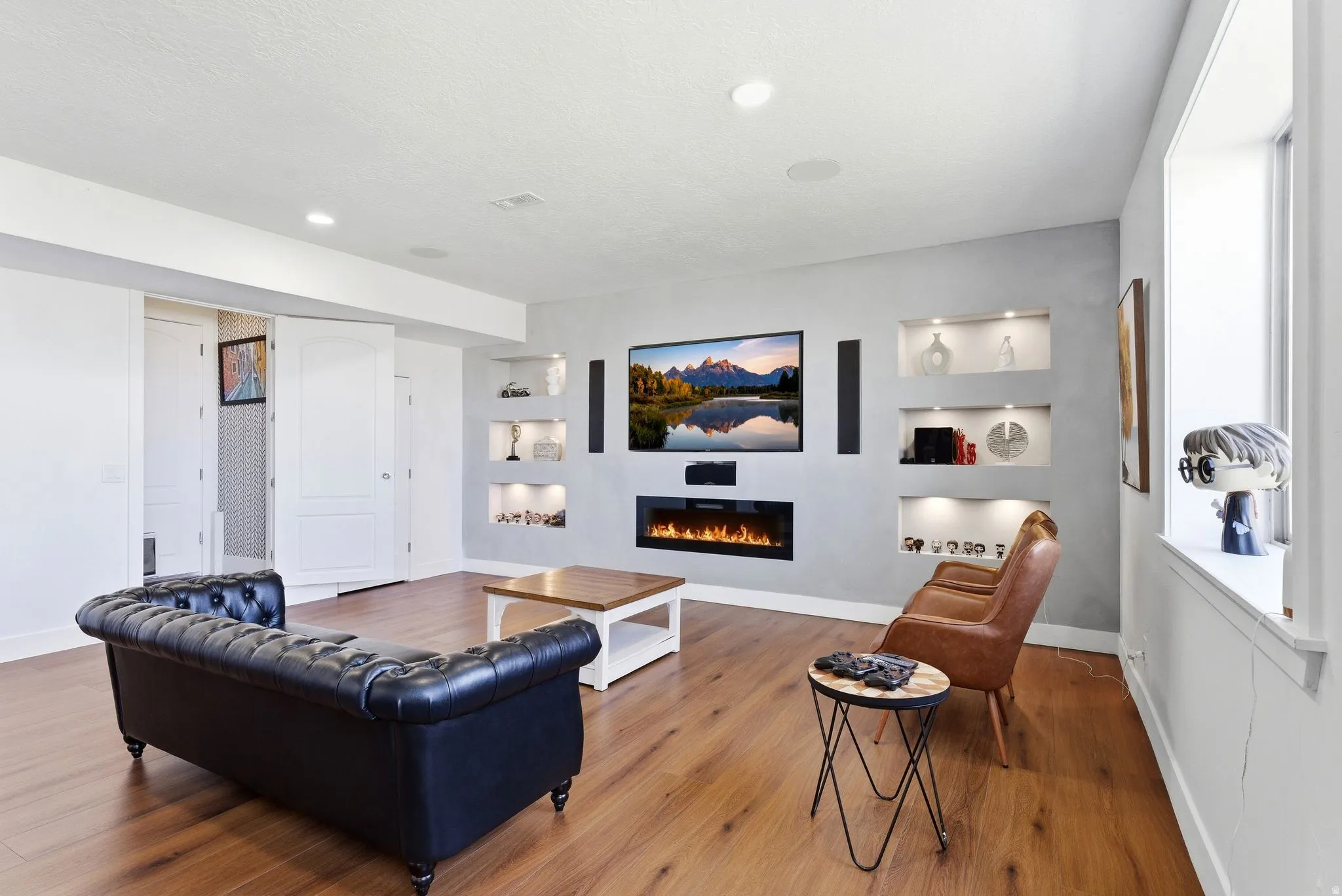 Living room featuring built in features, a glass covered fireplace, and wood finished floors