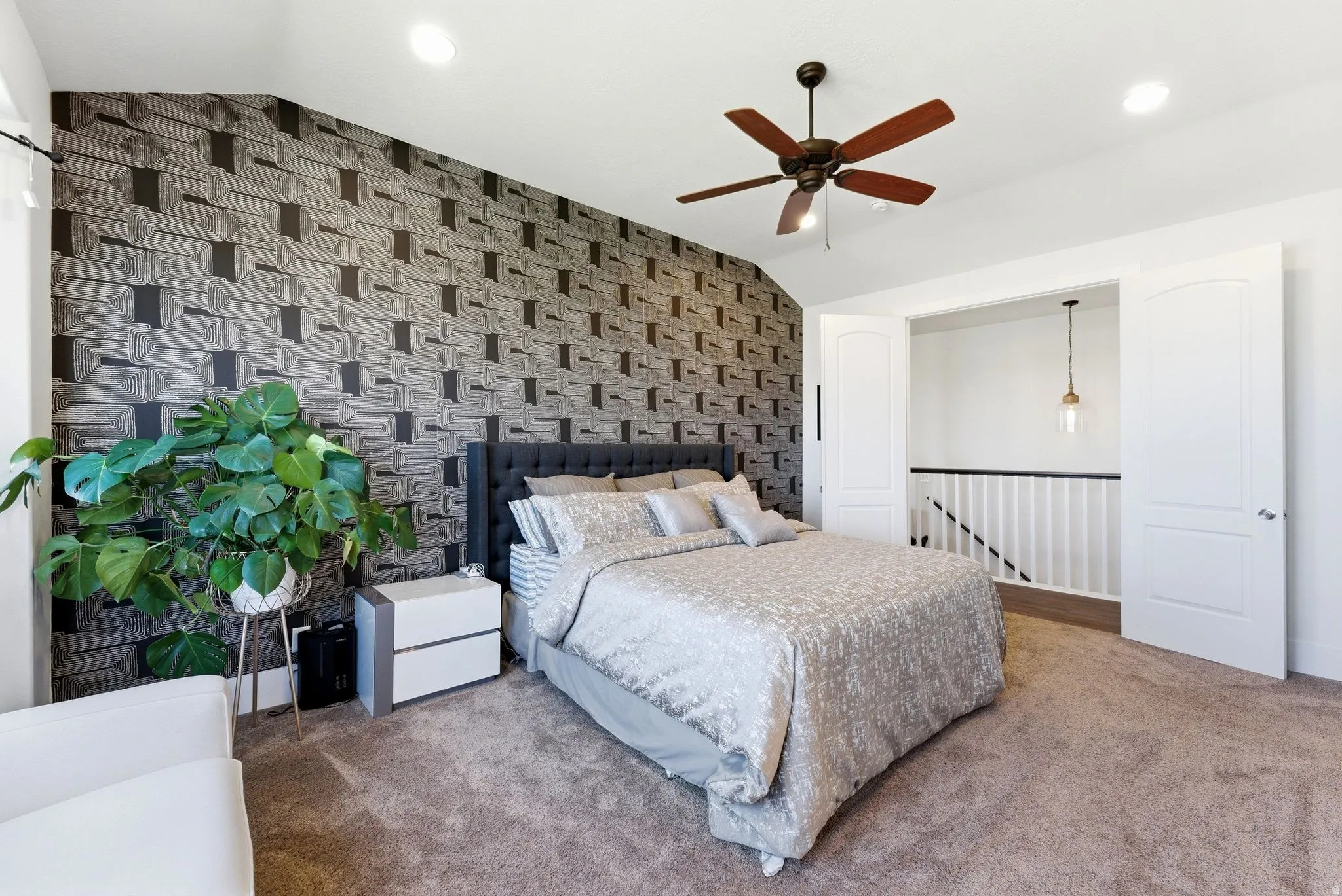 Carpeted bedroom featuring an accent wall, lofted ceiling, wallpapered walls, and a ceiling fan