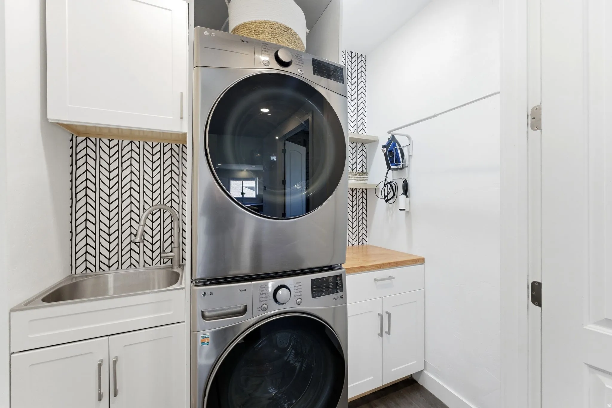 Laundry area featuring cabinet space, stacked washer and clothes dryer, and dark wood-type flooring