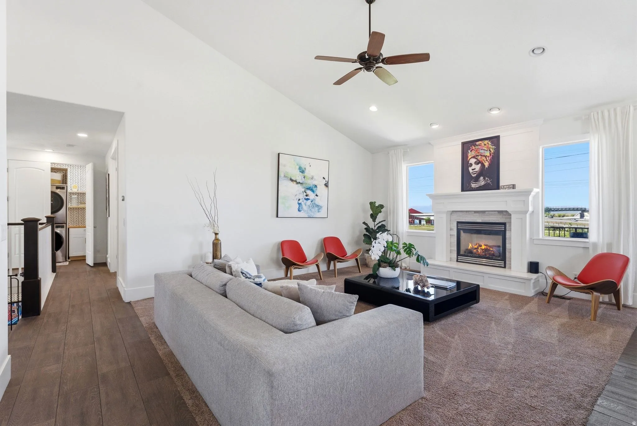 Living room with stacked washer / drying machine, dark wood finished floors, ceiling fan, healthy amount of natural light, and lofted ceiling