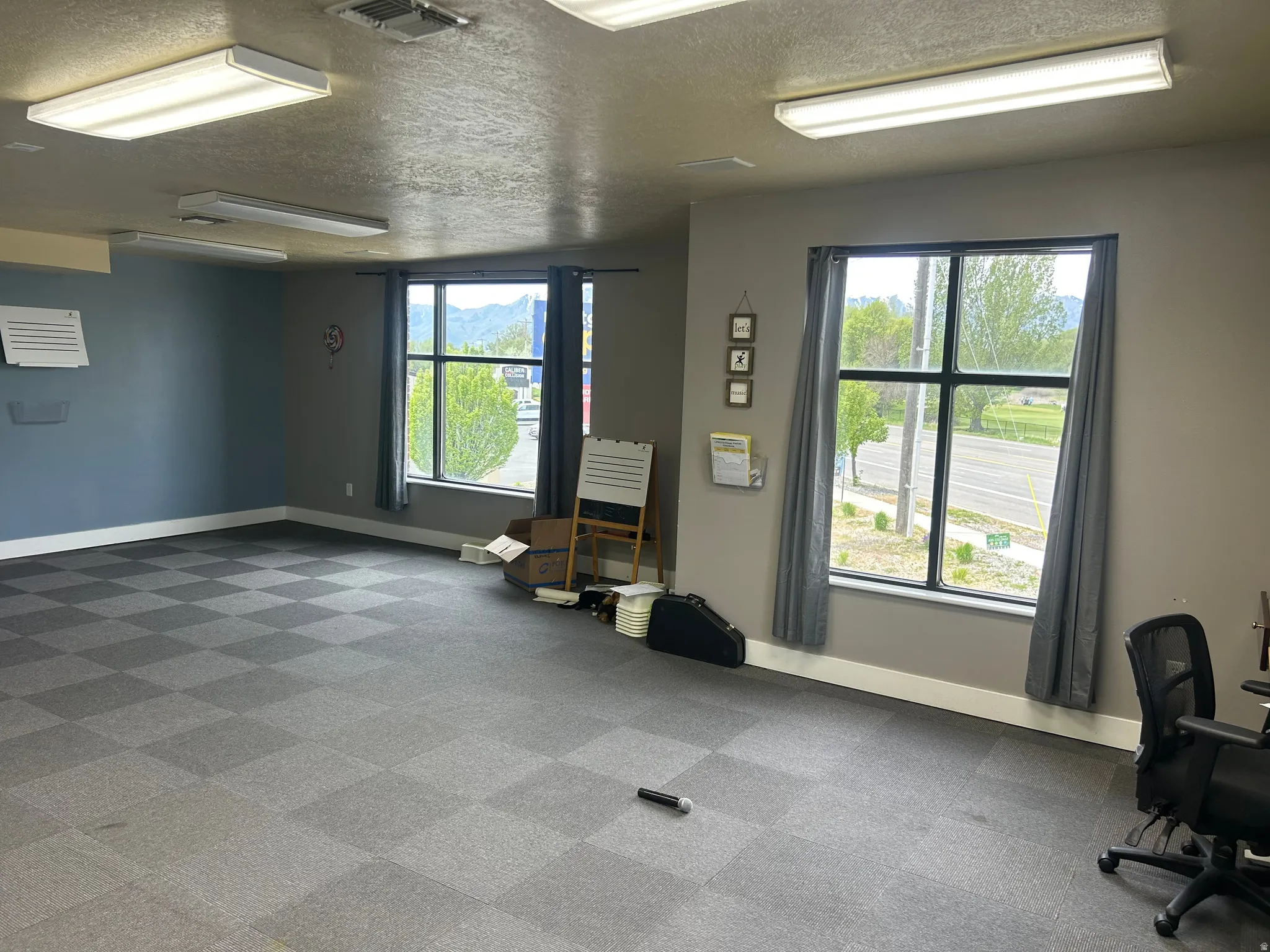 Spacious interior featuring checkerboard carpet flooring, multiple windows providing ample natural light, and overhead fluorescent lighting fixtures