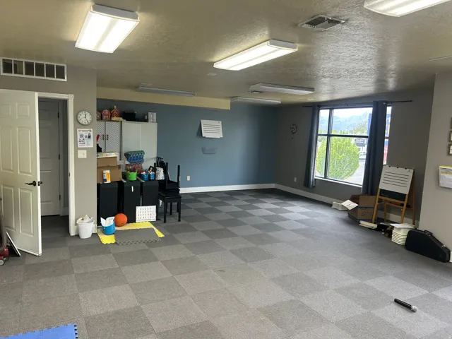 Spacious room featuring checkered carpet tile flooring, a large window, and multiple fluorescent ceiling lights