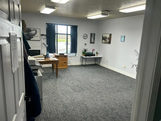 Spacious room featuring broadloom carpeting, light gray walls, white baseboards, and multiple fluorescent ceiling light fixtures