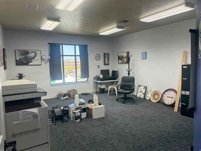 Spacious room featuring ceiling-mounted fluorescent lighting, a large window, light-colored walls, and textured carpet flooring