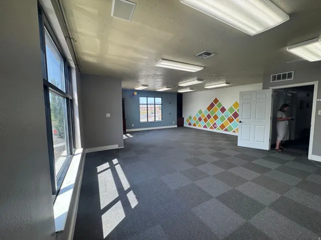 Spacious room featuring checkered gray carpet flooring, a decorative accent wall with a geometric pattern, and multiple large windows
