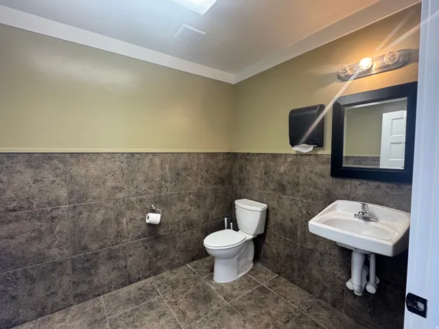 Restroom featuring dark stone-look tile flooring and wainscoting, white wall-mounted sink, and a white toilet