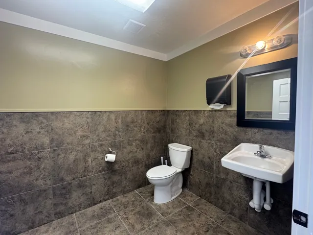 Restroom featuring floor-to-ceiling tile, pedestal sink with chrome faucet, wall-mounted mirror, and overhead lighting