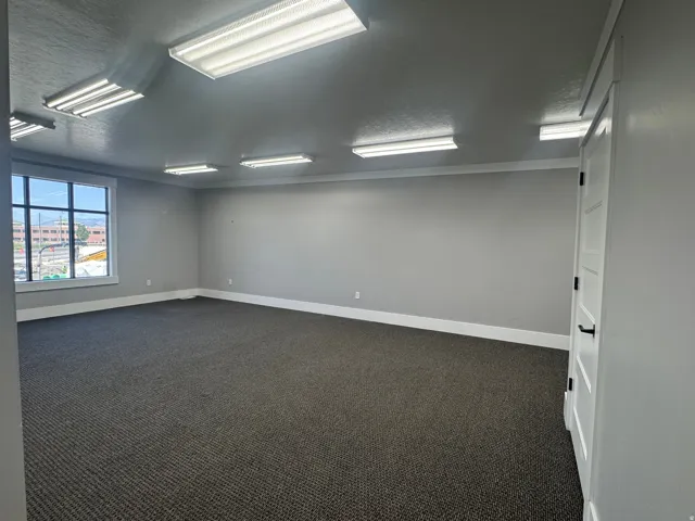 Spacious room featuring neutral grey walls and dark patterned carpeting