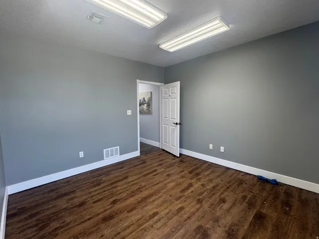 Room featuring wood-finish flooring, neutral gray walls, white baseboards, and overhead fluorescent lighting