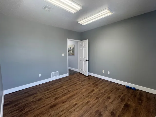 Room featuring wood-finish flooring, neutral gray walls, bright overhead fluorescent lighting, and white baseboards