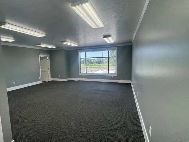 Spacious room featuring broadloom carpet, multiple overhead fluorescent light fixtures, and a large window