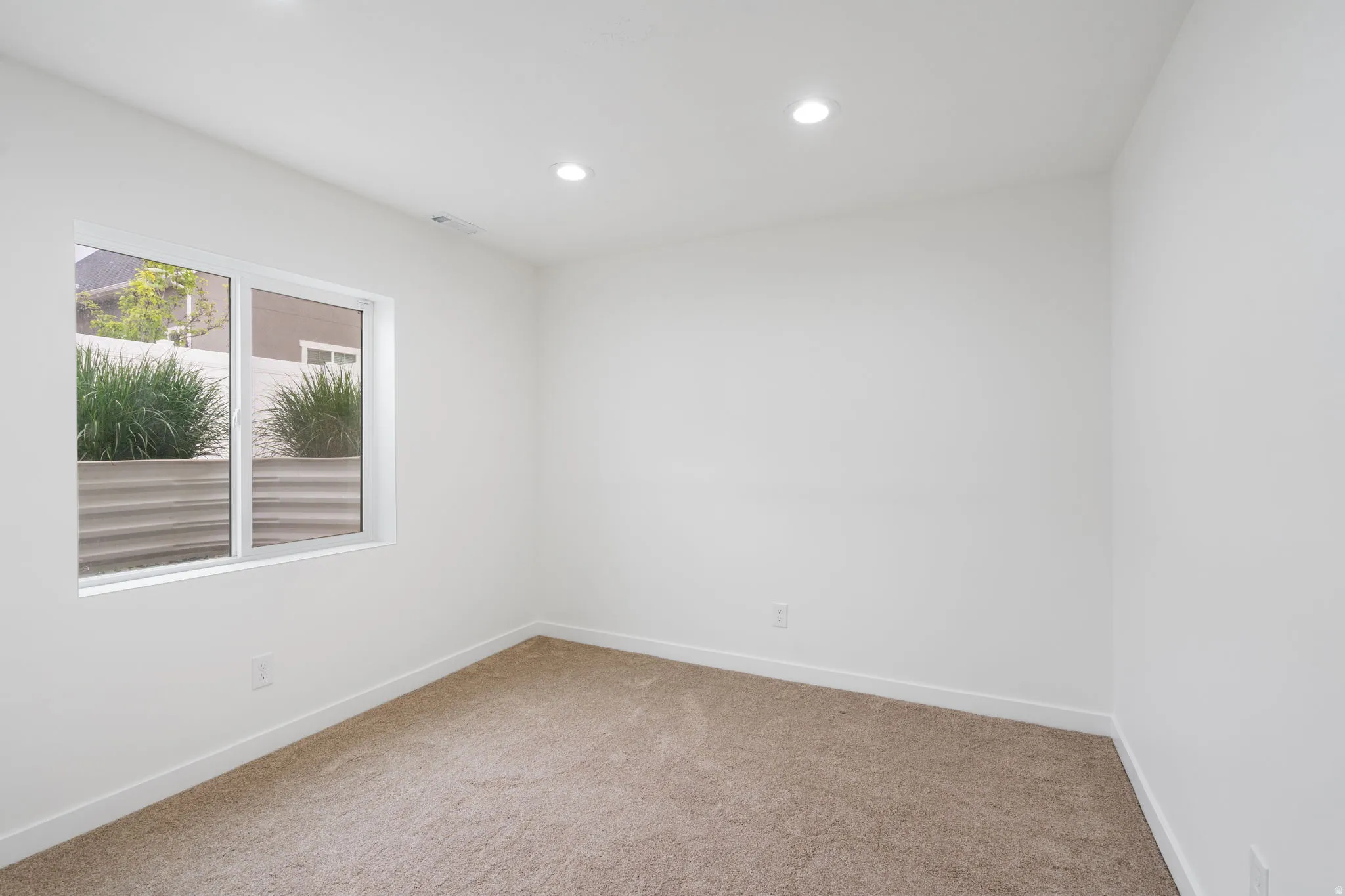 Bright room featuring white walls, recessed lighting, a large window, light brown carpet, and white baseboards