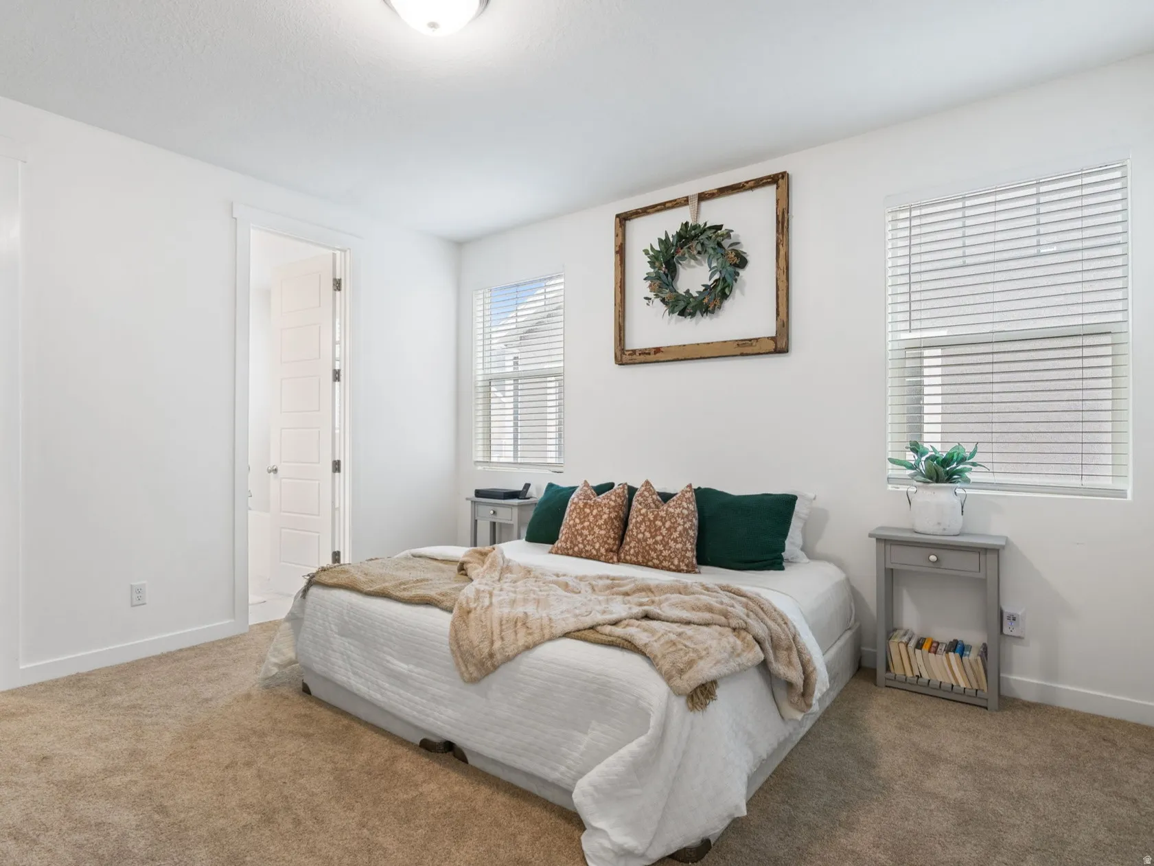 Carpeted bedroom featuring white walls, dual windows with blinds, a ceiling-mounted light fixture, and a walk-in closet with built-in shelving