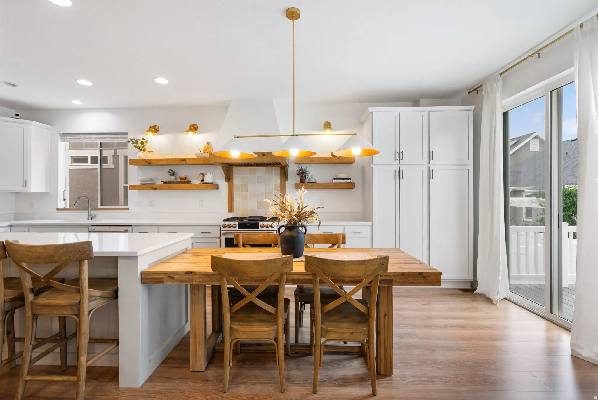 Modern kitchen featuring white cabinetry, light wood-finish flooring, a white island with seating, a gold pendant light fixture, and sliding glass doors to the exterior