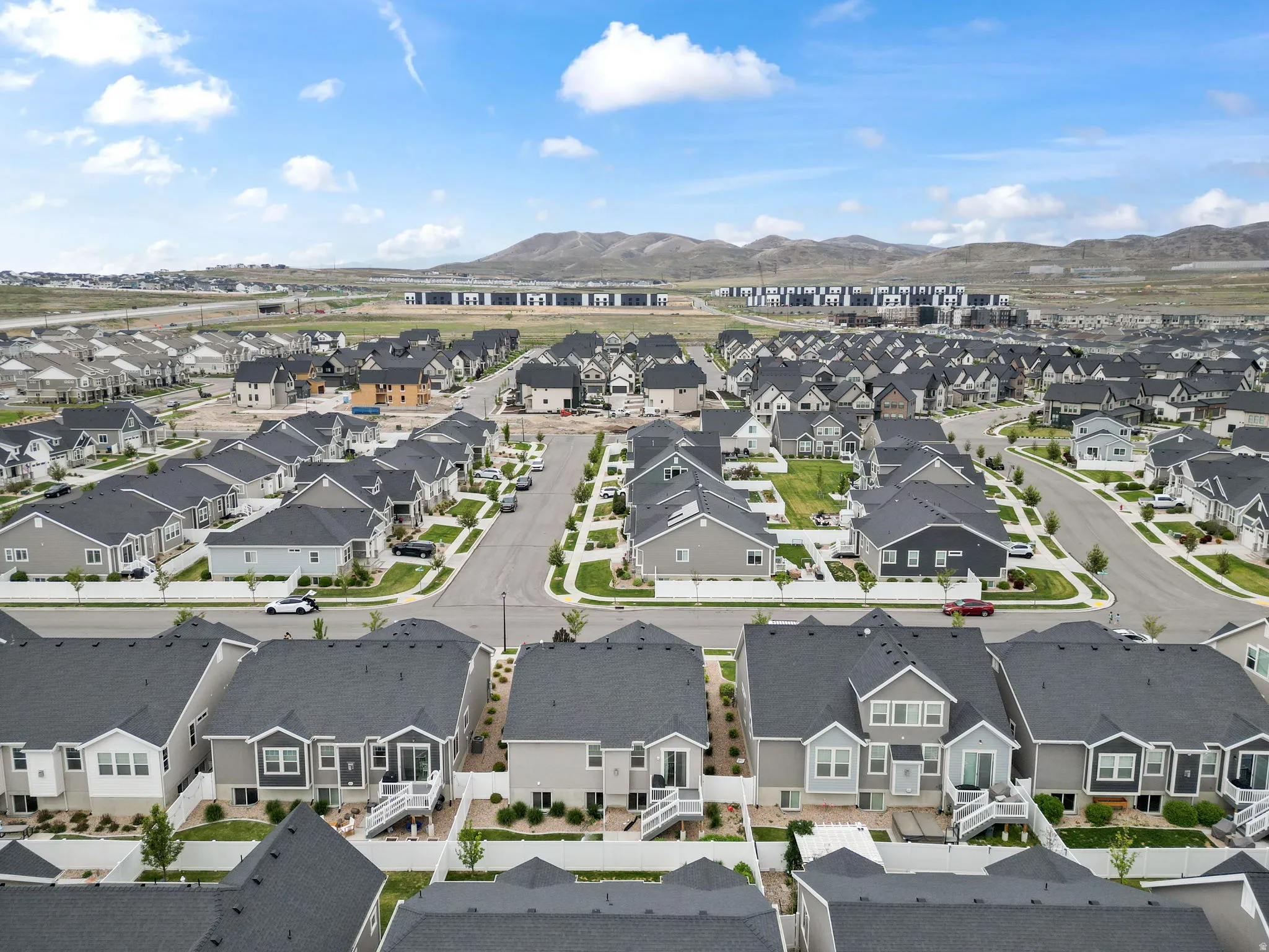 Expansive residential development featuring modern homes with dark shingle roofs, landscaped yards, and white fencing