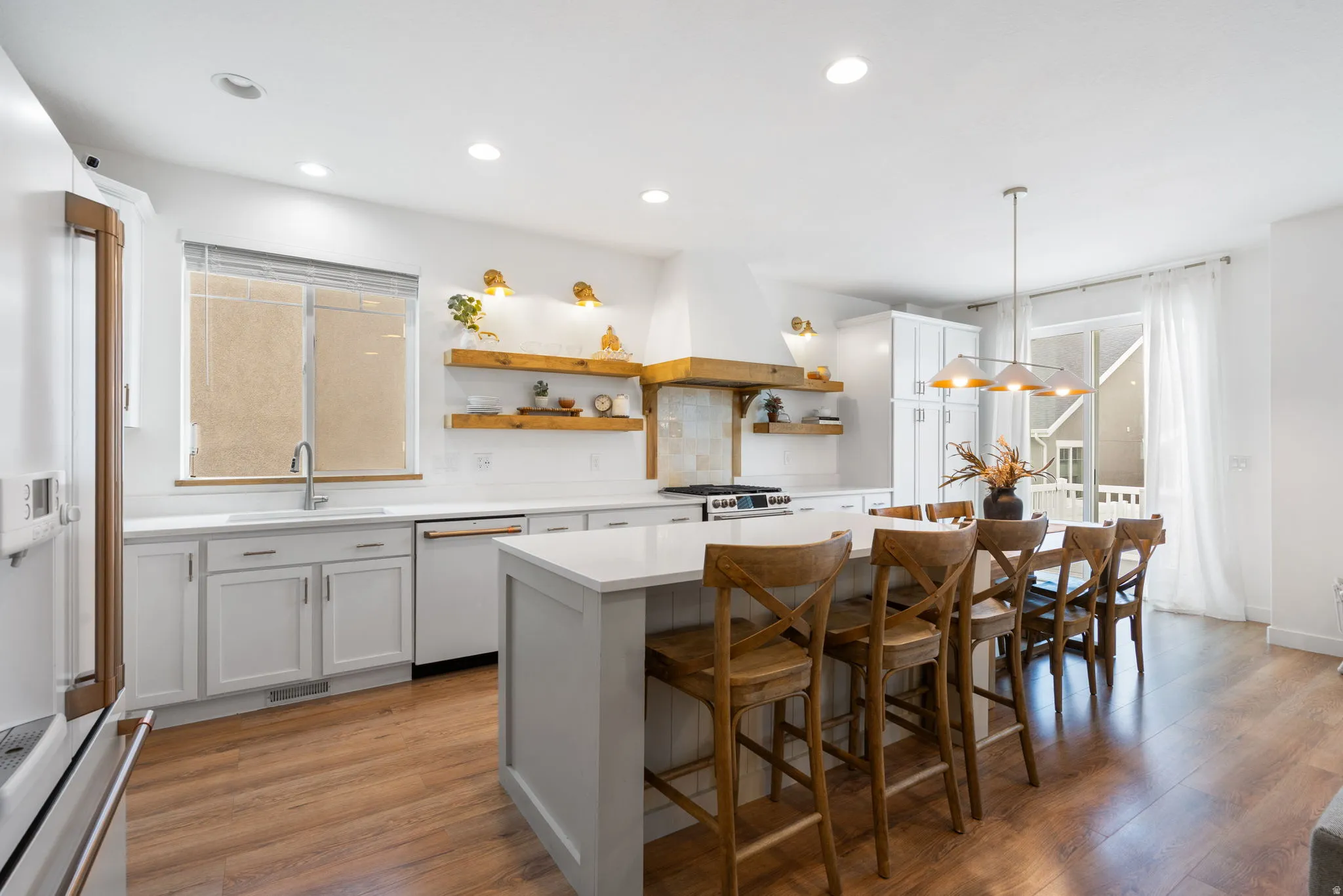 Spacious kitchen featuring white shaker cabinetry, light countertops, wood-finish flooring, a central island with seating, and a sliding glass door