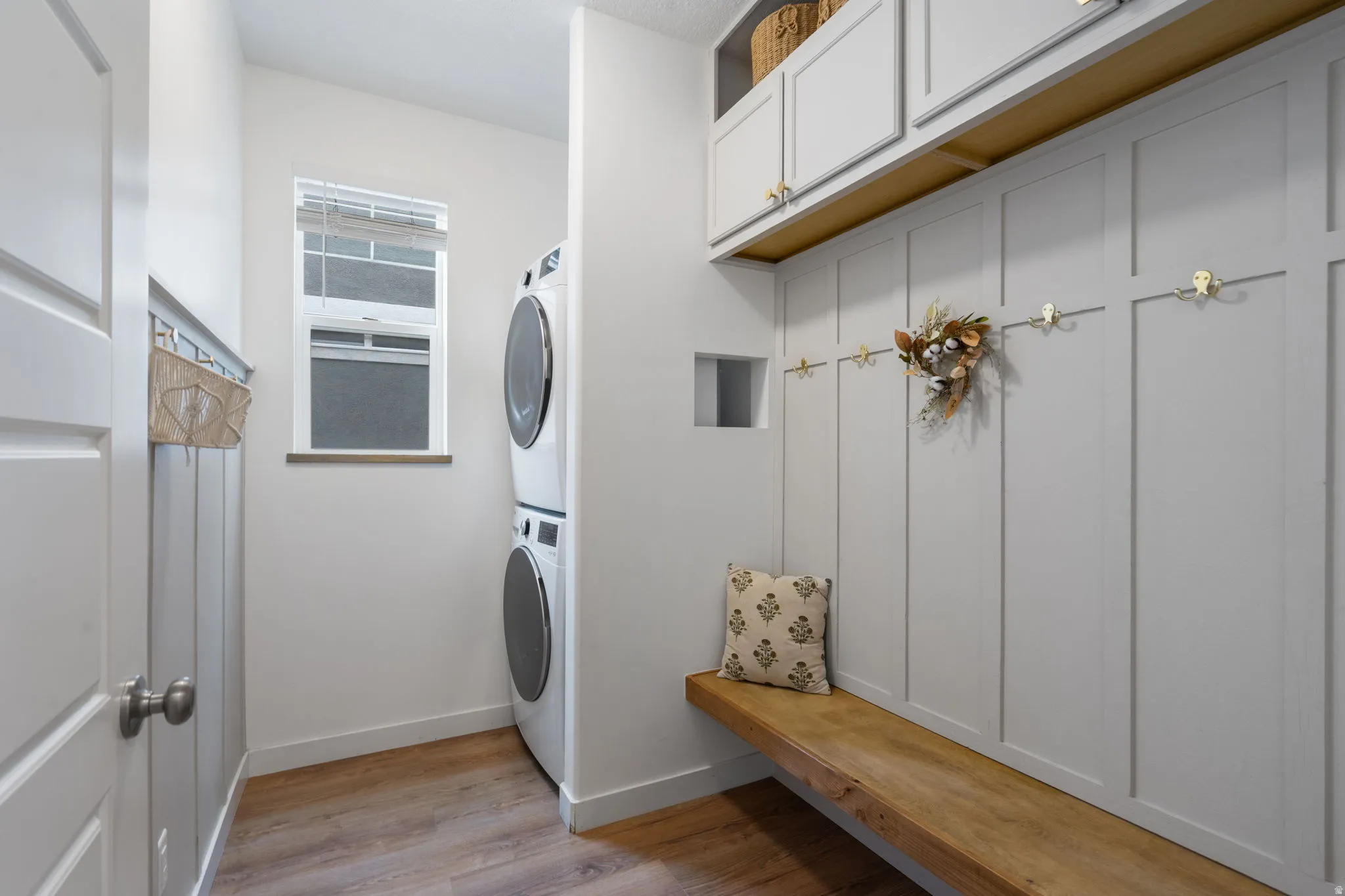 Mudroom featuring a built-in wooden bench, vertical wall paneling, and upper cabinetry