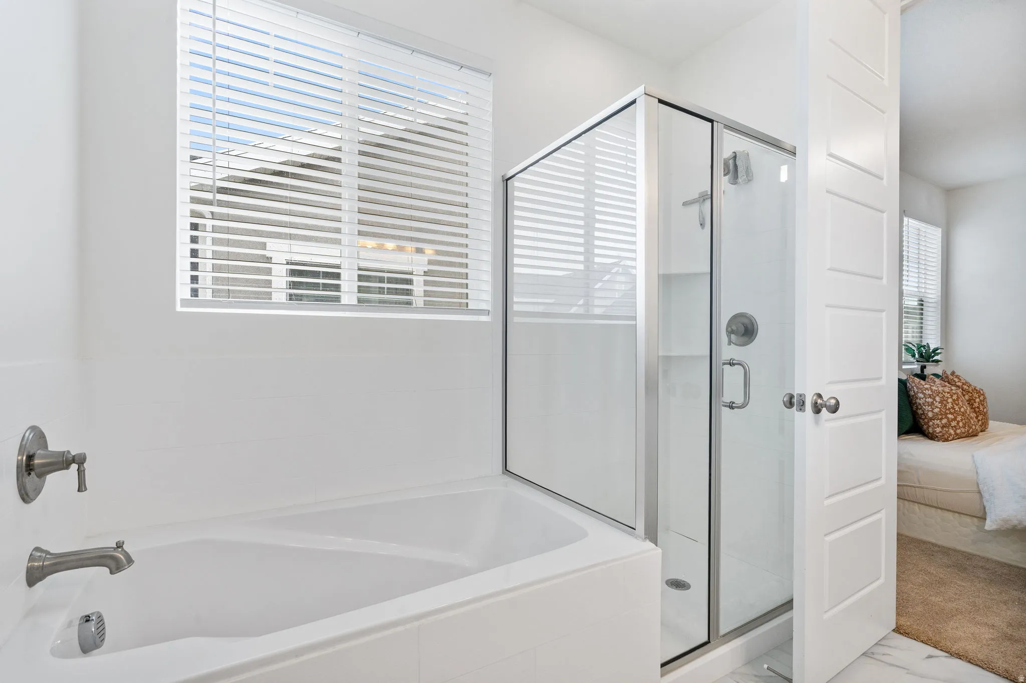 Contemporary bathroom featuring a white soaking tub with brushed nickel fixtures, a glass-enclosed shower, white tile flooring, and a window with blinds