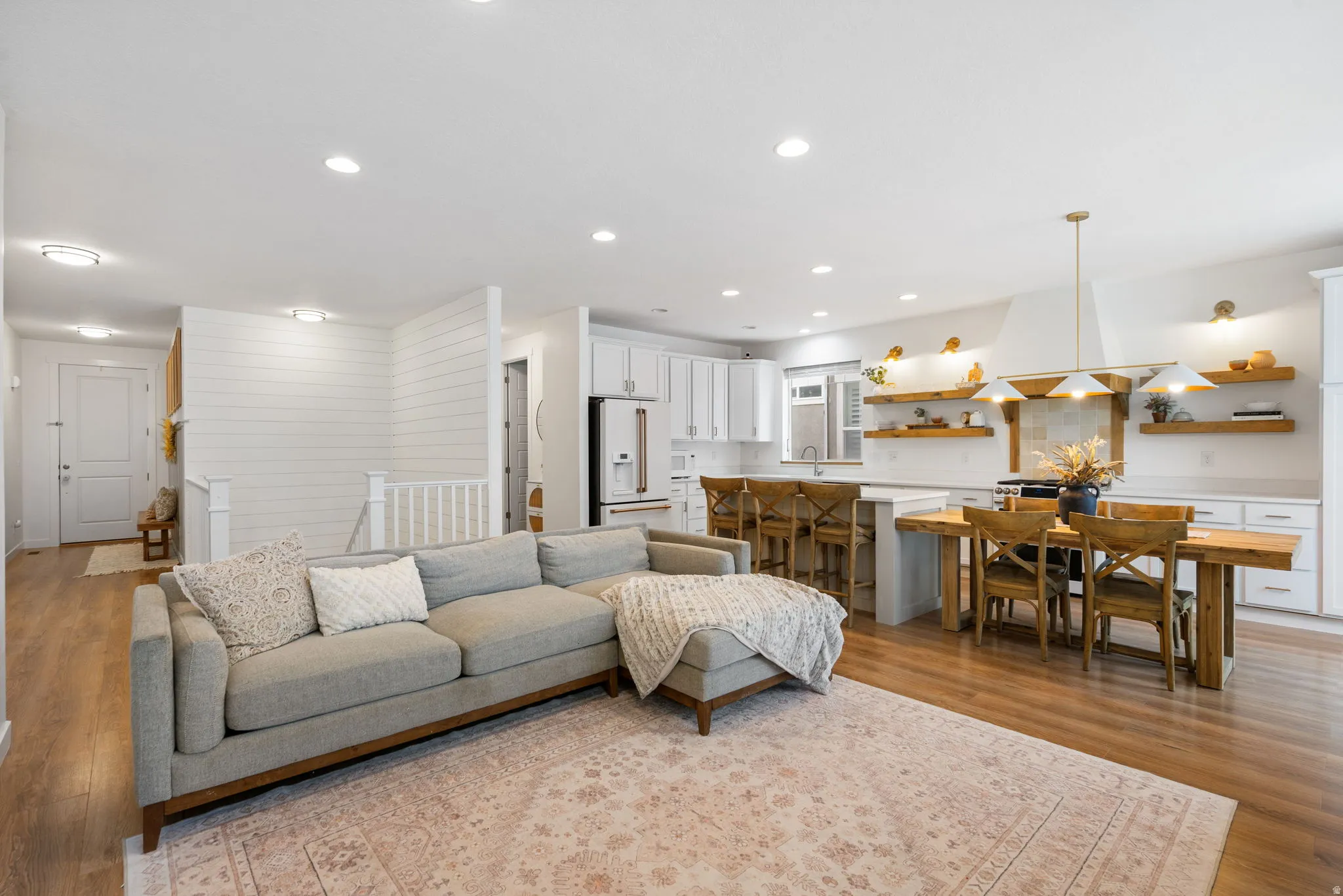 Open-concept living area featuring wood-finish flooring, recessed lighting, white shiplap wall accents, white cabinetry, and an eat-at kitchen island