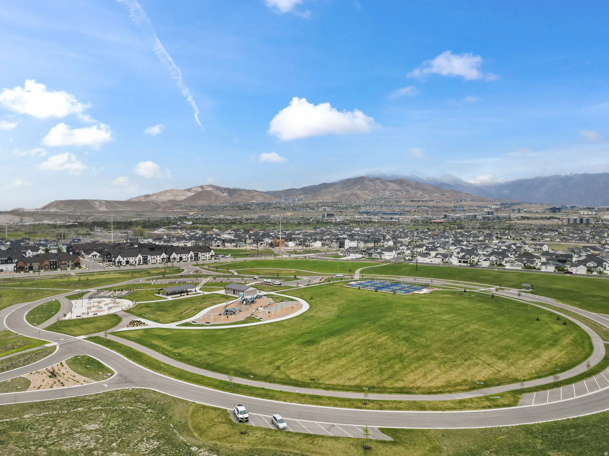 Expansive green spaces featuring paved pathways, recreational fields, a playground area, and distant mountain backdrops