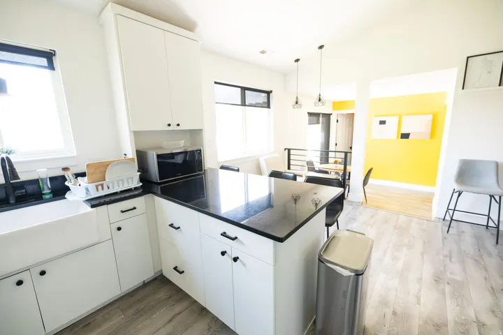 Kitchen with dark wood-style floors, white cabinetry, a peninsula, decorative light fixtures, and black microwave