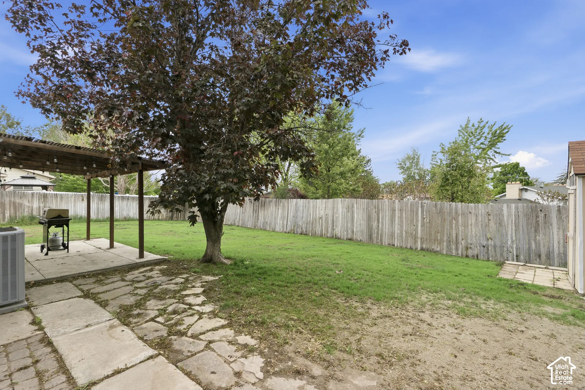 Expansive backyard featuring a manicured lawn, a mature shade tree, a covered patio area, a concrete slab, and a full privacy fence