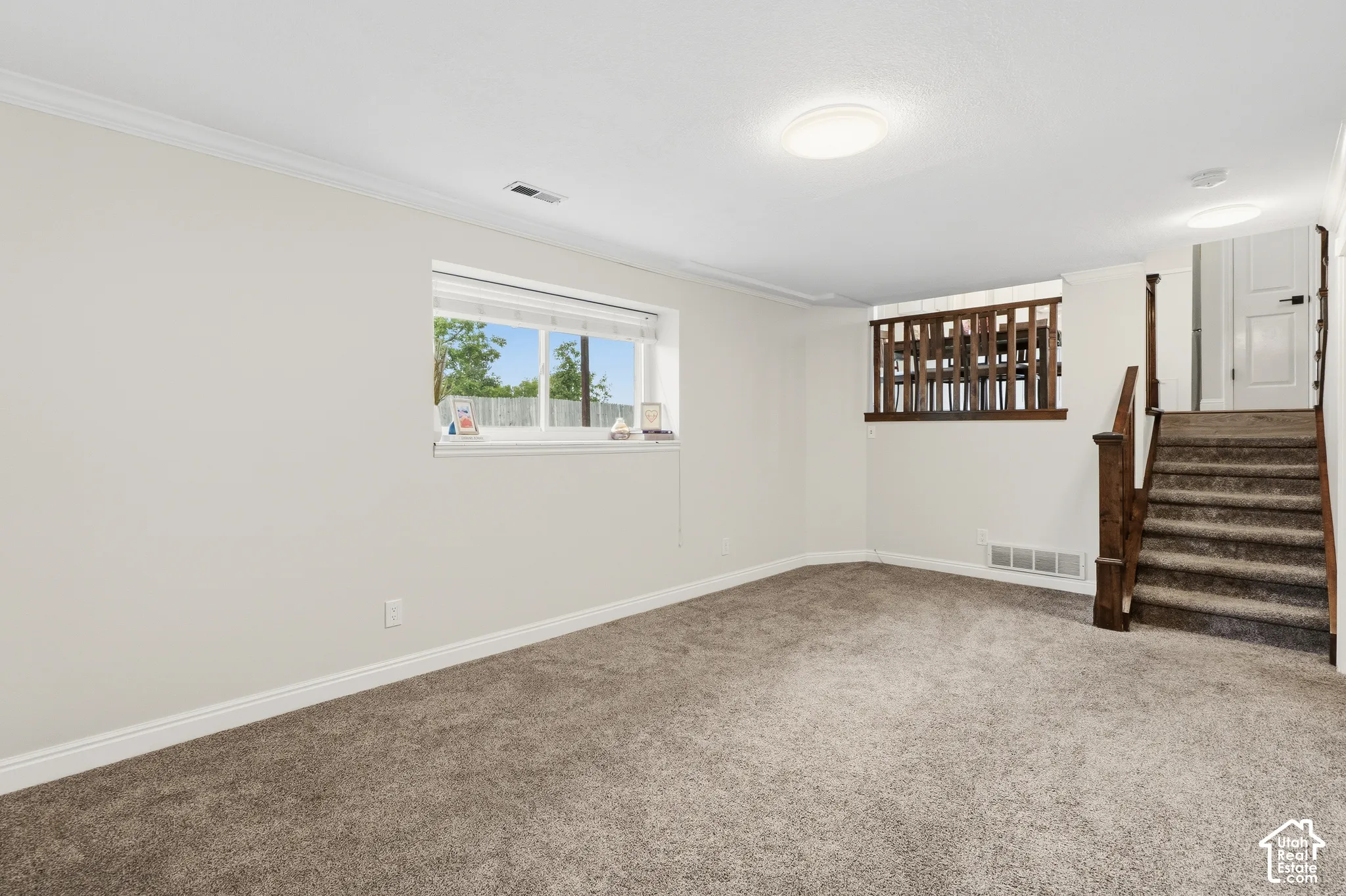 Spacious room featuring neutral carpeting, a large window, white baseboards, and crown molding
