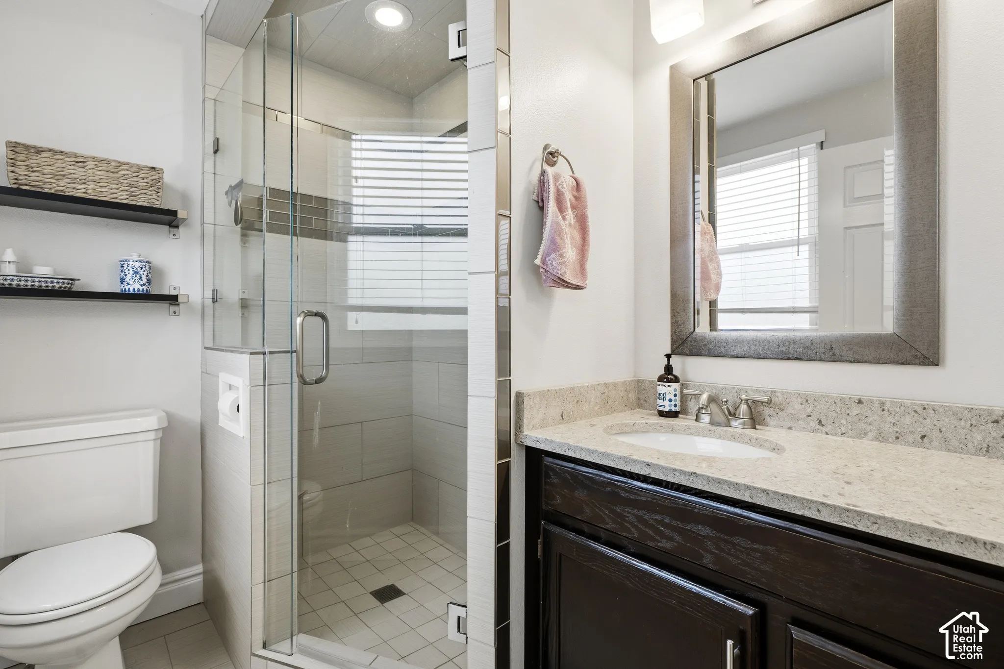 Contemporary bathroom featuring a glass-enclosed shower with tile surround and integrated shelving, a dark wood-finish vanity with a light-toned countertop, and a framed mirror