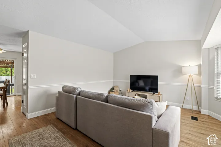 Spacious living area featuring wood-finish flooring, vaulted ceiling, and chair rail molding
