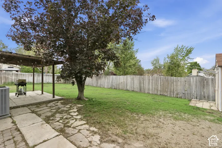 Expansive backyard featuring a manicured lawn, a mature shade tree, a covered patio area, a concrete slab, and a full privacy fence