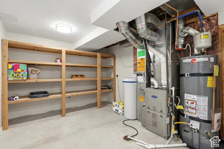 Basement utility space featuring a water heater, furnace, water softener, and extensive built-in wooden shelving for organized storage