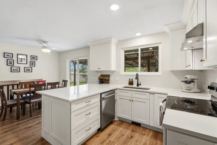 Bright kitchen featuring white shaker cabinetry, stainless steel appliances, a center island with countertop seating, wood-finish flooring, and a subway tile backsplash