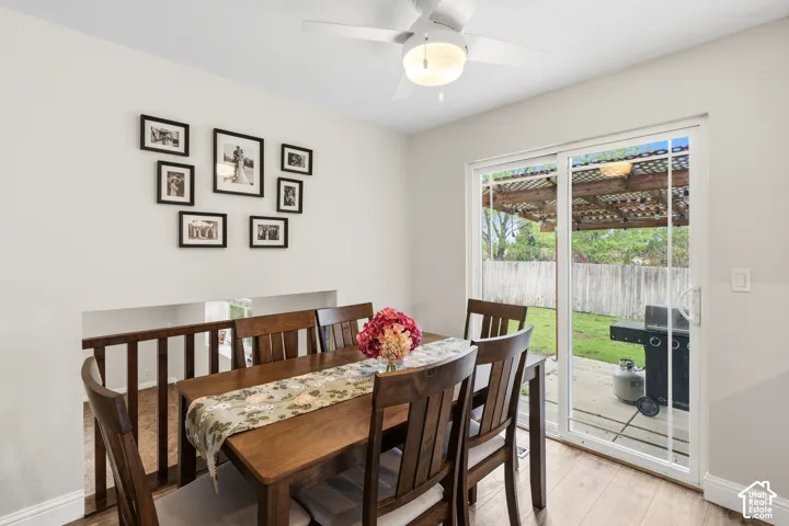 Dining area featuring wood-finish flooring, a ceiling fan with integrated lighting, and a half-wall with wood railing
