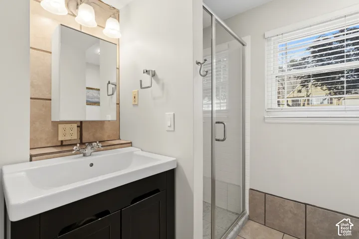 Bathroom featuring a dark wood-finish vanity with an integrated white sink, a glass-enclosed shower, a wall-mounted medicine cabinet, and a window with horizontal blinds