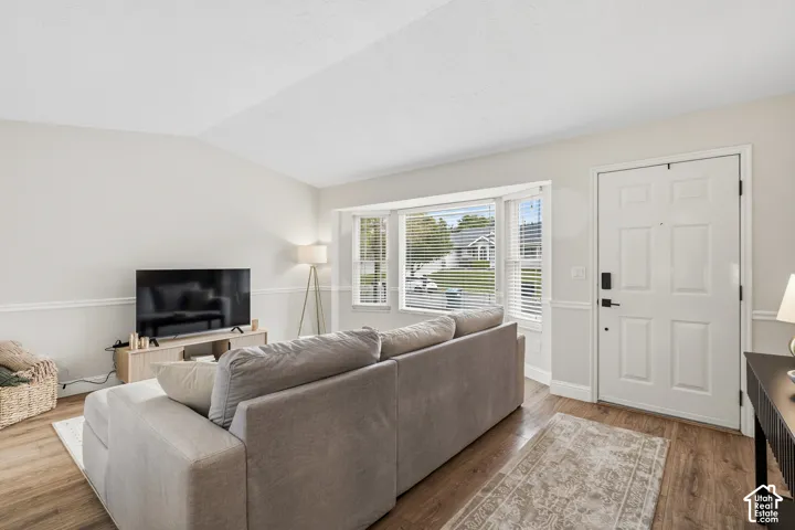 Living area featuring wood-finish flooring, a white paneled front entry door, and a bay window with horizontal blinds