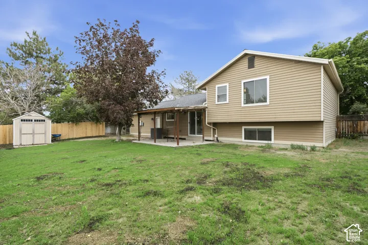 Expansive green lawn with a wooden privacy fence, a detached shed, a mature tree, and a covered patio area