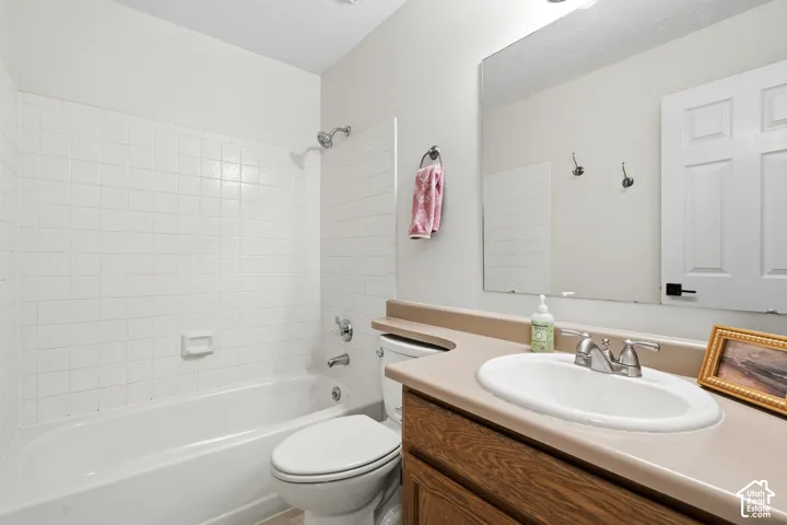 Full bathroom featuring a white porcelain tub with shower, white tile surround, and a vanity with a wood-finish cabinet and integrated sink