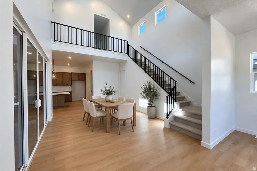 Vaulted ceiling, wood-finish flooring, glass sliding doors, open-riser staircase with metal railing, and upper-level windows