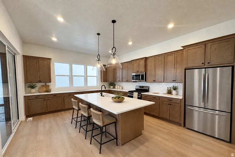 Gourmet kitchen featuring wood-finish cabinetry, stainless steel appliances, a center island with seating, a tile backsplash, and multiple windows